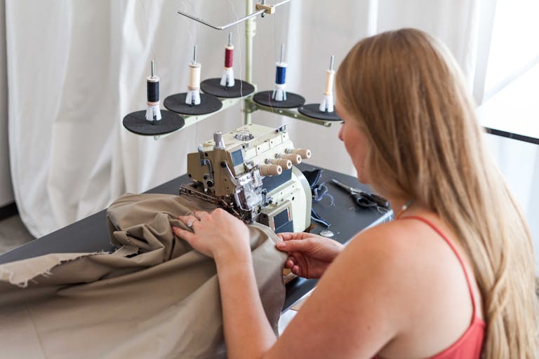 A woman sewing fabric using a sewing machine in a studio setting.