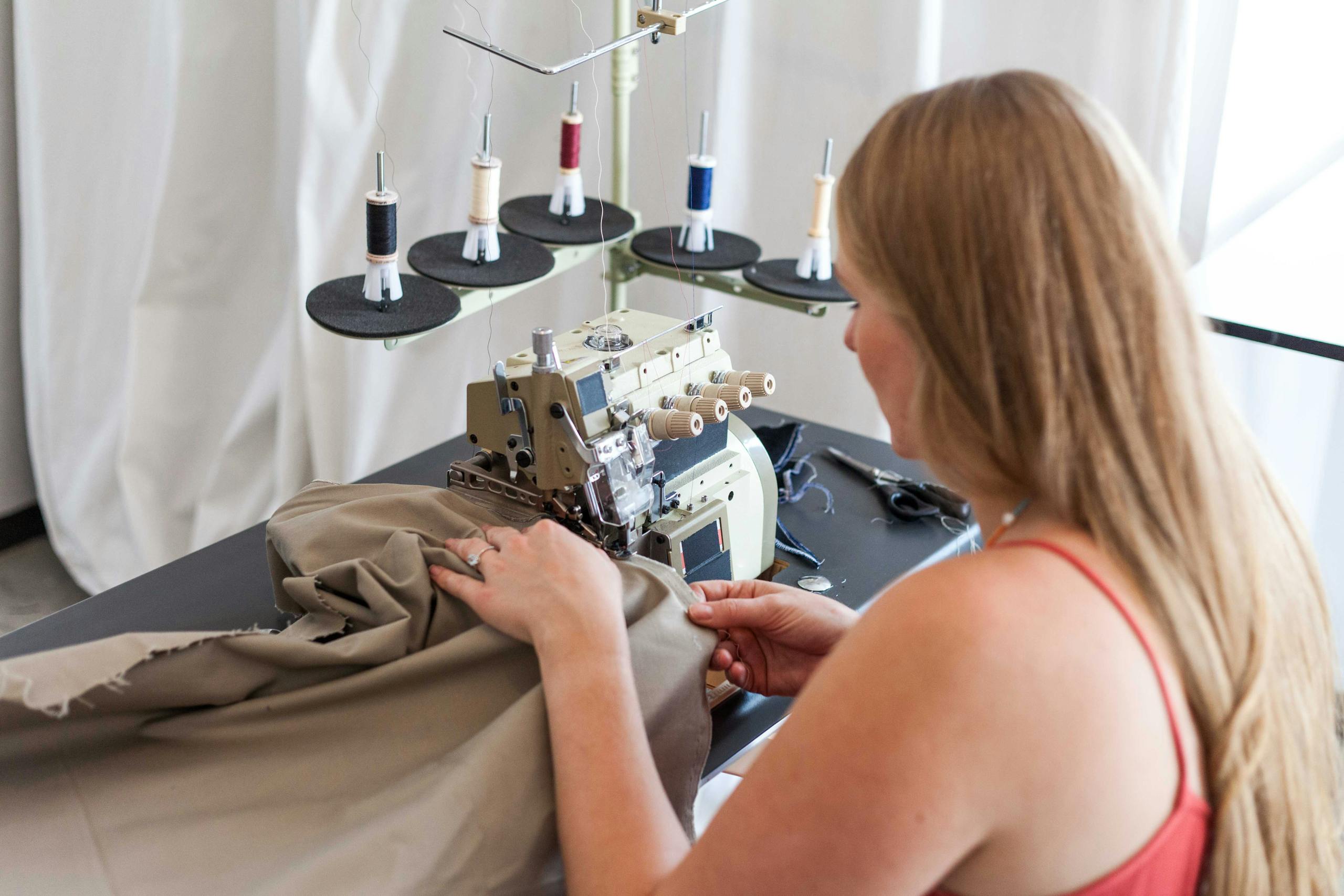 A woman sewing fabric using a sewing machine in a studio setting.