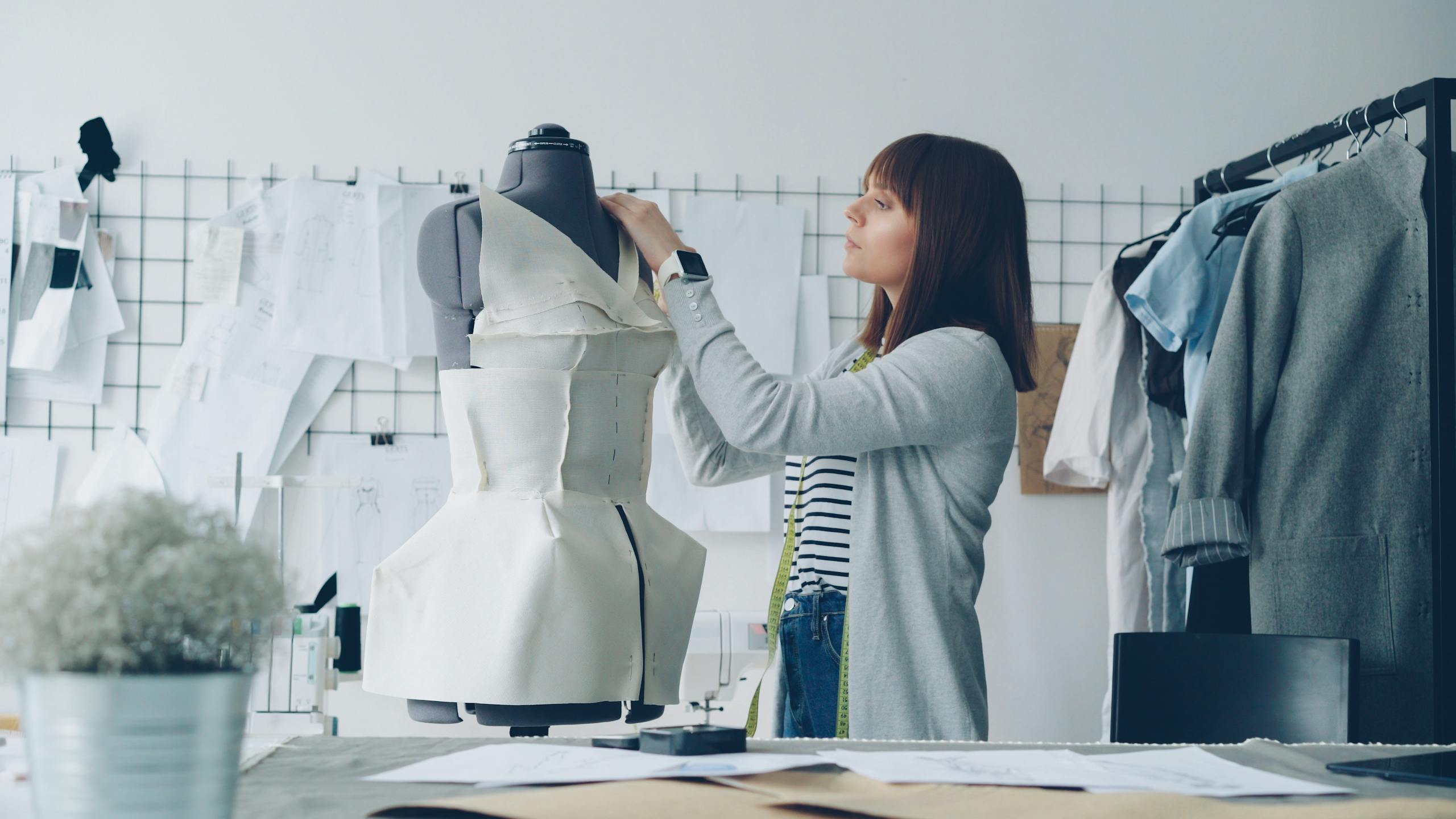 Fashion designer adjusting a dress on a mannequin in a studio filled with sketches.