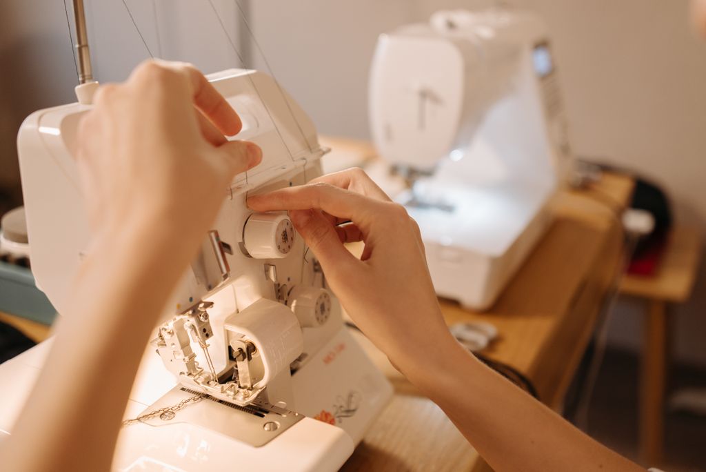 Hands adjusting knobs on a sewing machine for precise stitching. Perfect for sewing, crafting, or hobby-related visuals.